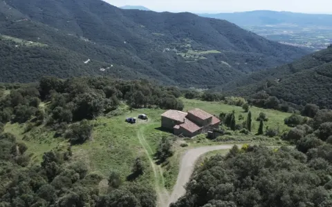 Stone farmhouse in a clearing among forested mountains.