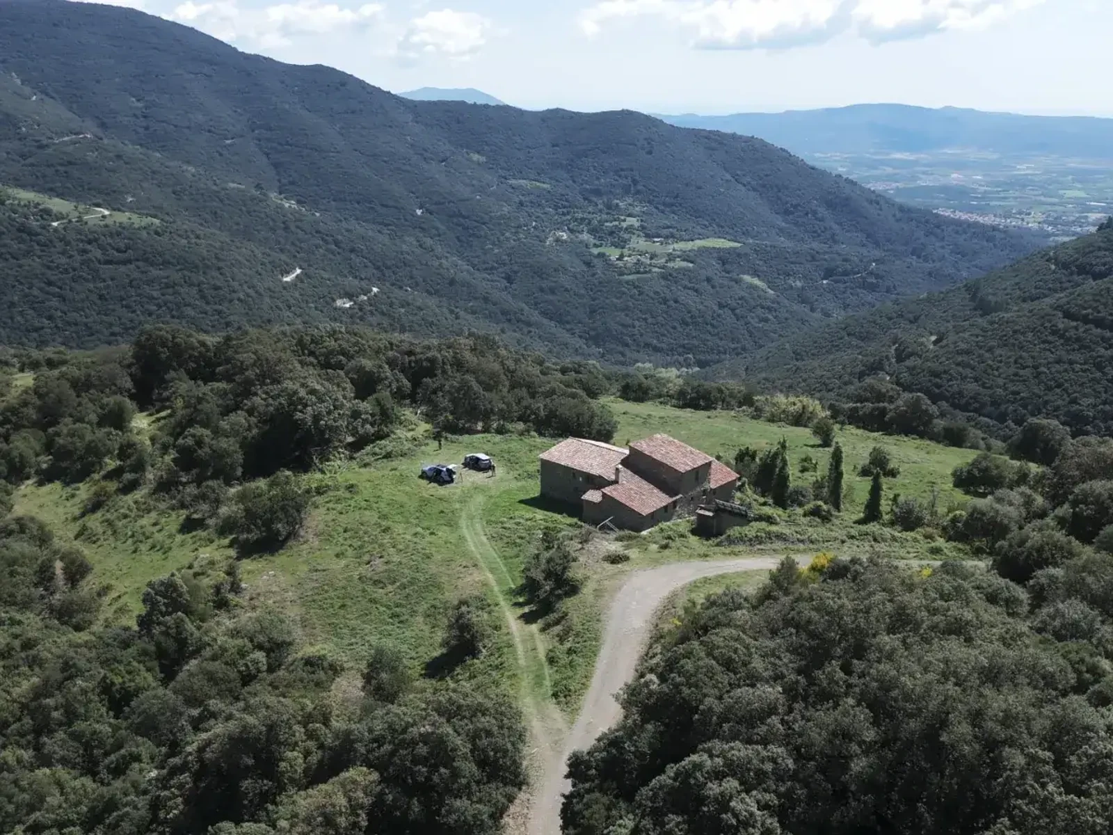 Stone farmhouse in a clearing among forested mountains.
